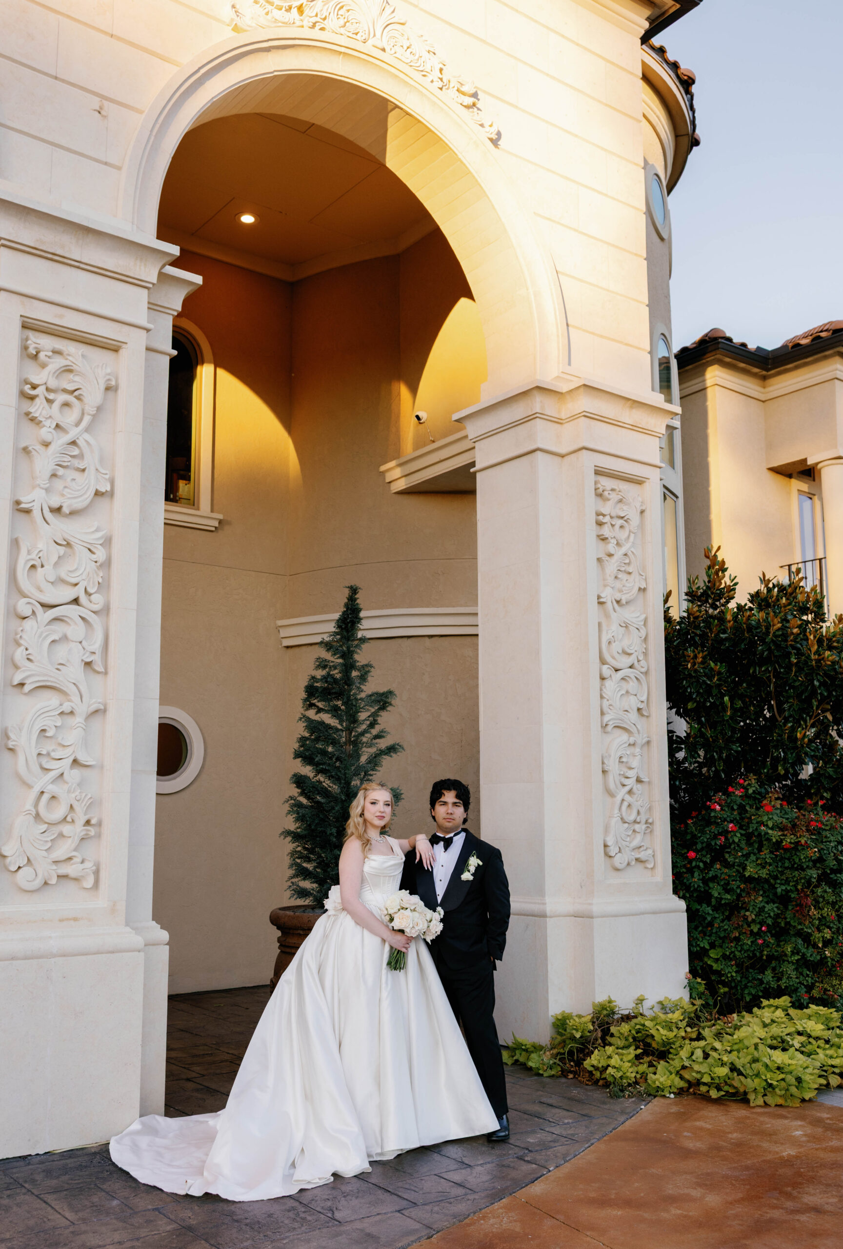 Bride and groom embracing in front of white columns at the entrance of D’Vine Grace Vineyard in McKinney, Texas